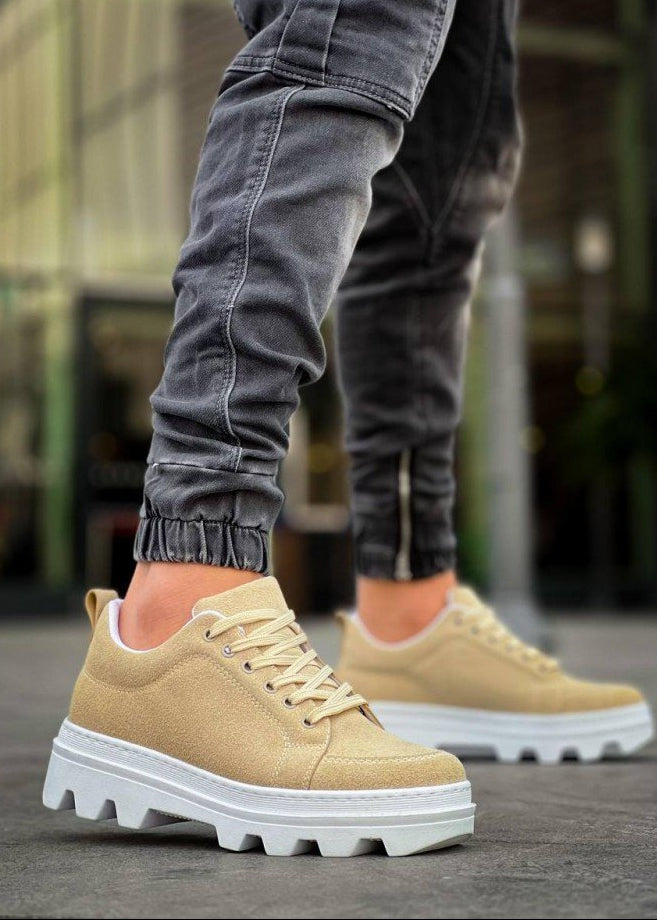 Beige sneakers with white soles worn by a person on a blurred background